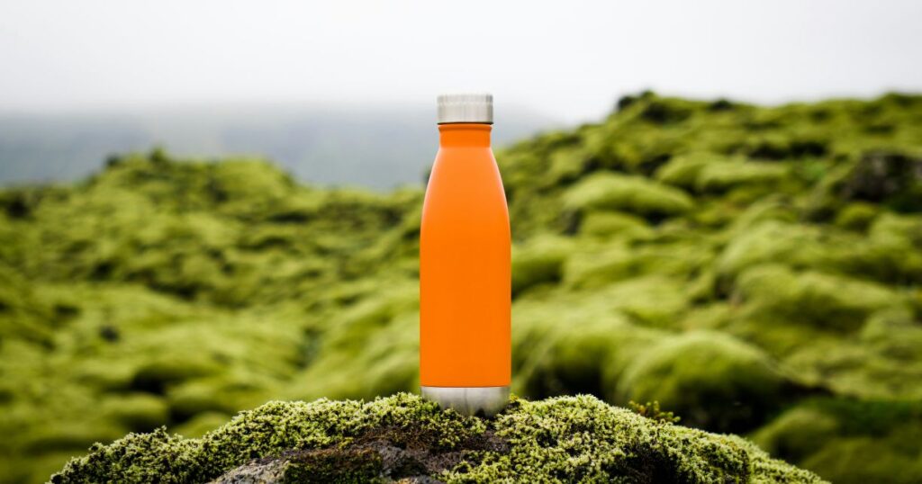 Orange water bottle at a green hill in rainy day