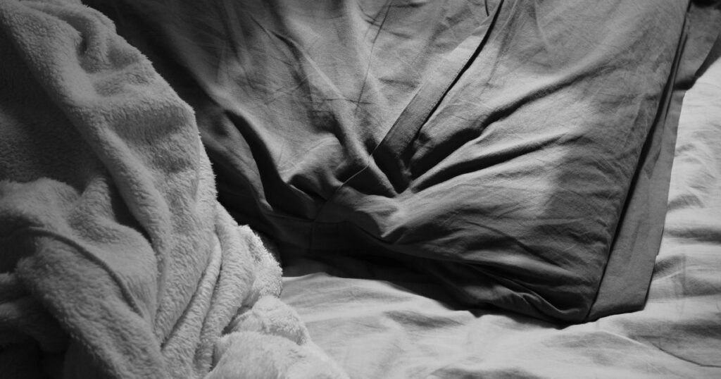 grey bedsheet with blanket beside it